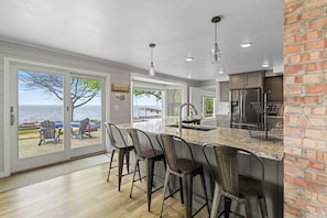 A kitchen with a large island, bar stools, a refrigerator, and a view of the sea.