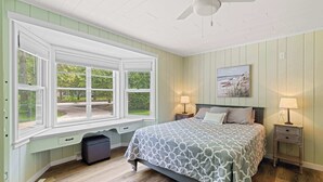 A bedroom with a large window, a bed with a patterned bedspread, two bedside tables with lamps, and a ceiling fan. - Egg Harbor home with waterfront access-Sleeps 12! (Egg Harbor)