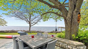 An outdoor patio with a table and chairs, a view of the sea, and a large tree. - Egg Harbor home with waterfront access-Sleeps 12! (Egg Harbor)