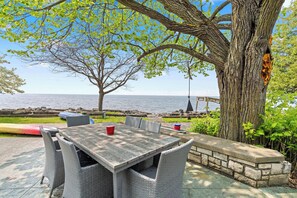 An outdoor patio with a table and chairs, a view of the sea, and a large tree. - Egg Harbor home with waterfront access-Sleeps 12! (Egg Harbor)