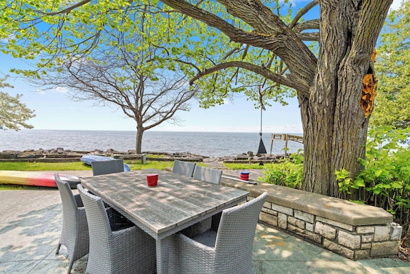 An outdoor patio with a table and chairs, a view of the sea, and a large tree.