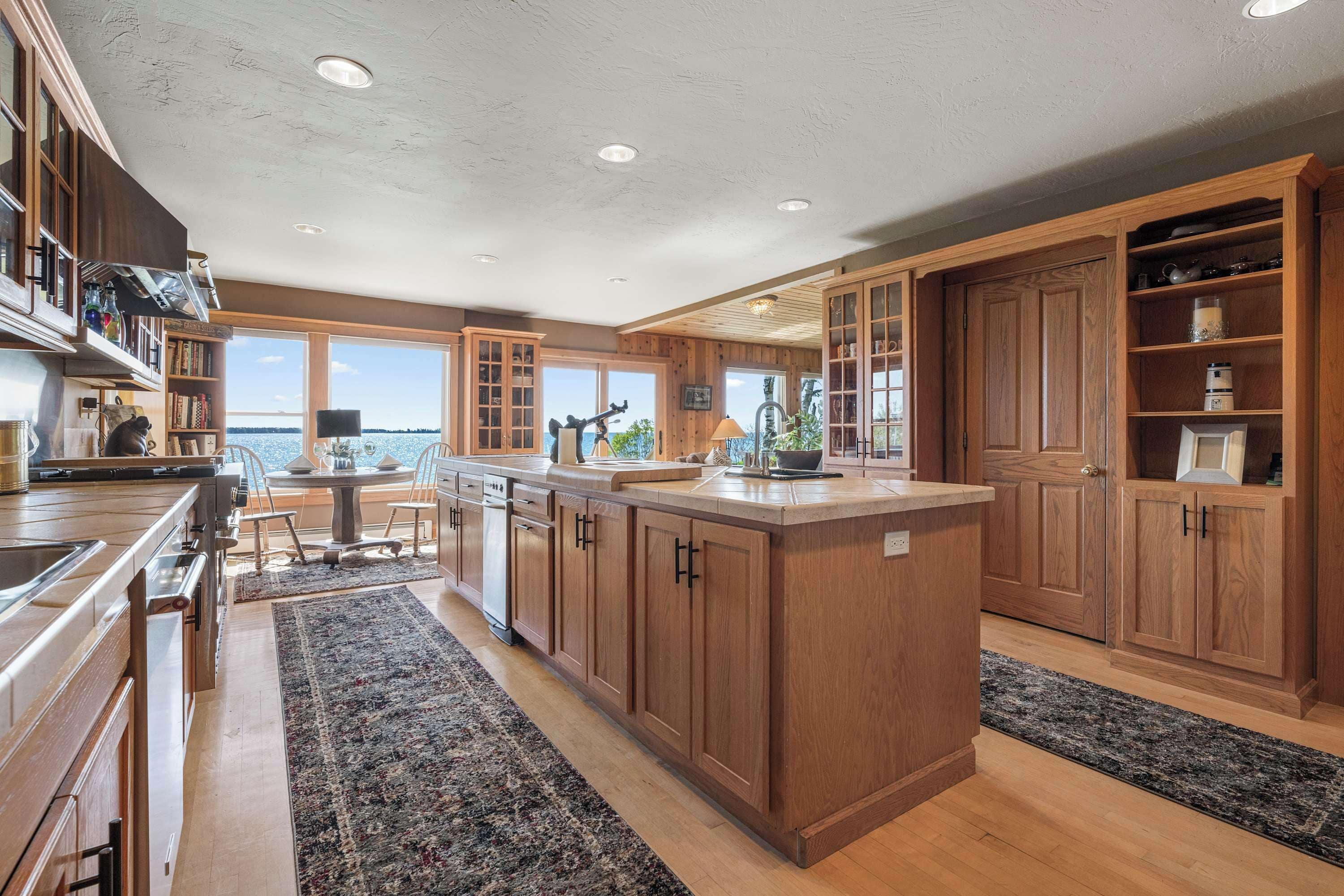 A spacious kitchen with wooden cabinets, a central island, and large windows offering a view of the water.