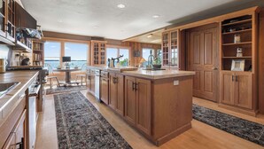 Una cocina amplia con armarios de madera, una isla central y ventanas grandes que ofrecen vistas al agua.
