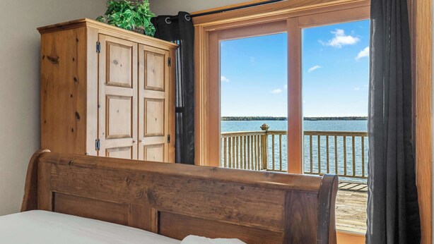 Un dormitorio con cabecera y armario de madera, y vistas a un balcón con barandilla y una masa de agua.
