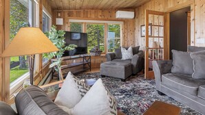 Una habitación con paneles de madera, un sofá, un reposapiés y un televisor.