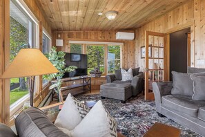 Ein Zimmer mit Holzwänden, einer Couch, einem Hocker und einem Fernseher.