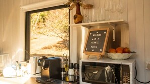 A kitchen with a coffee machine, a microwave, a sign reading 'WELCOME TO ARANYA ACRES,' and a window with a view of trees. - Blue Gum at Langdale 1 by Tiny Away (Bungendore)