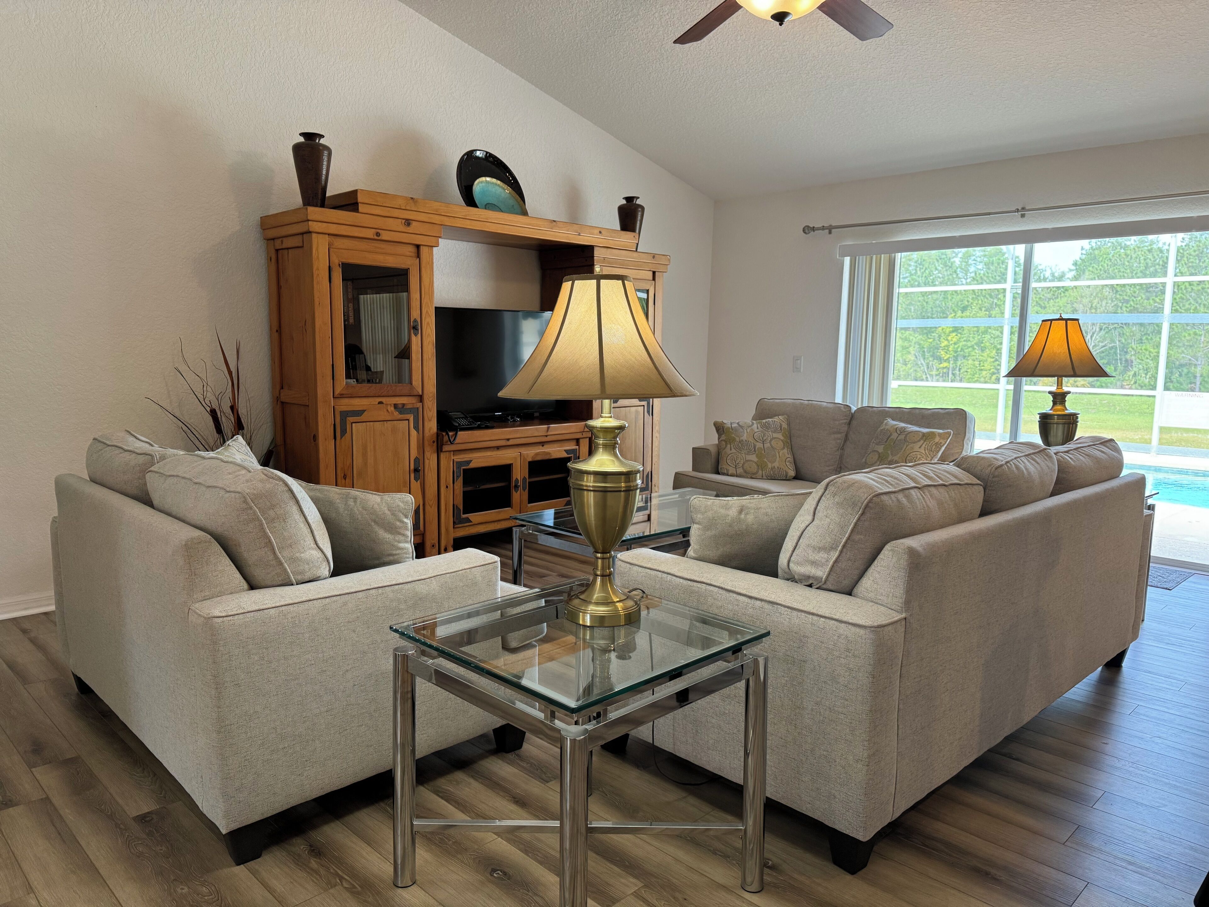 A living room with a glass coffee table, two sofas, a wooden entertainment unit, and a TV.