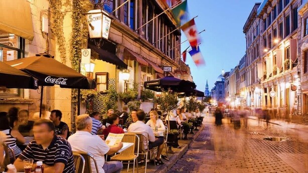A street with outdoor seating at cafes, a cobblestone path, and flags.