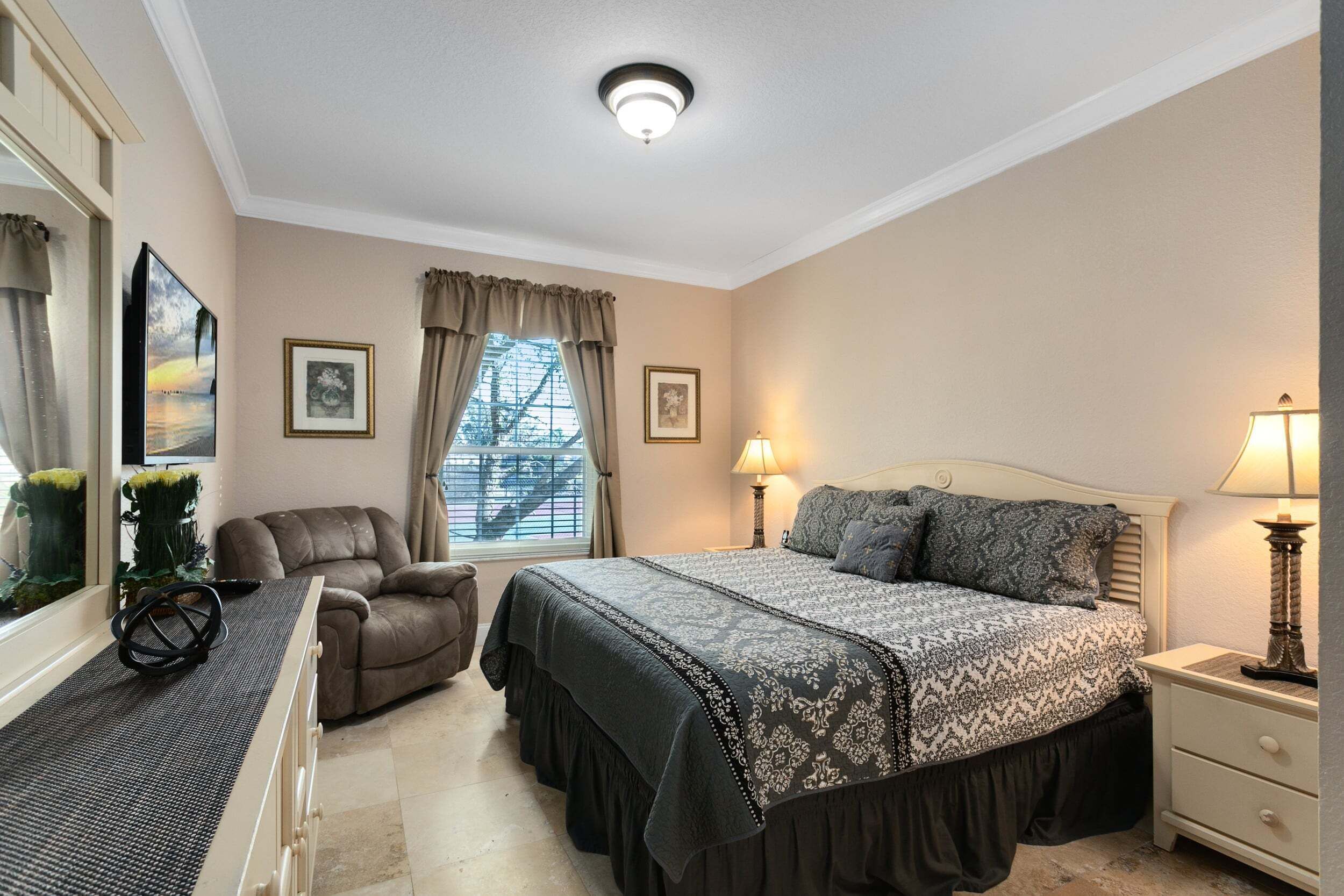 A hotel room with a bed, a chair, a desk, and a window with curtains.