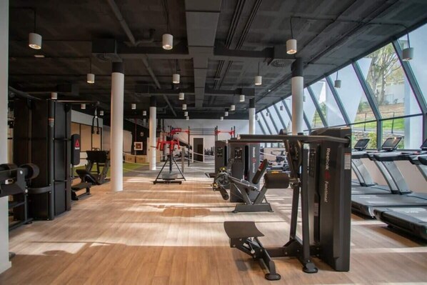 Ein Fitnessstudio mit Trainingsgeräten, Laufbändern und großen Fenstern.
