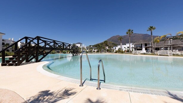 A swimming pool with a metal ladder, a bridge, and palm trees in the background. - Mirador Hills 2 | Estepona Luxury Apartment Pools (Estepona)