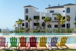 Ein Poolbereich mit bunten Adirondack-Stühlen und einem Gebäude mit weißer Fassade und schwarzen Fenstern.