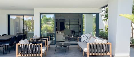 Un espacio exterior moderno para disfrutar al aire libre, con mesa de comedor, varias opciones de asientos y vistas hacia un espacio interior conectado.