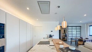 A modern kitchen with a marble countertop, pendant lights, and a dining area with a round table and chairs. - Mirador Hills 2 | Estepona Luxury Apartment Pools (Estepona)