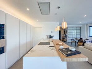 A modern kitchen with a marble countertop, pendant lights, and a dining area with a round table and chairs. - Mirador Hills 2 | Estepona Luxury Apartment Pools (Estepona)