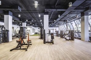 Ein geräumiges Fitnessstudio mit verschiedenen Trainingsgeräten, großen Fenstern und einer hohen Decke.