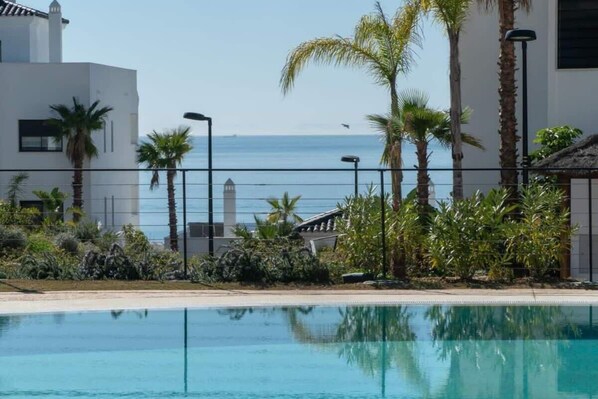 A pool with clear blue water, surrounded by palm trees and a building with a white facade.