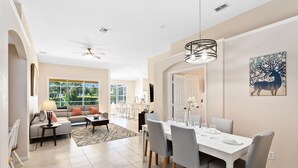 A spacious living room with a dining area, large windows, and a ceiling fan. - Last Minute Disney! Private Pool, Game Room & Themed Bedrooms. Book Now! #64097 (Orlando)