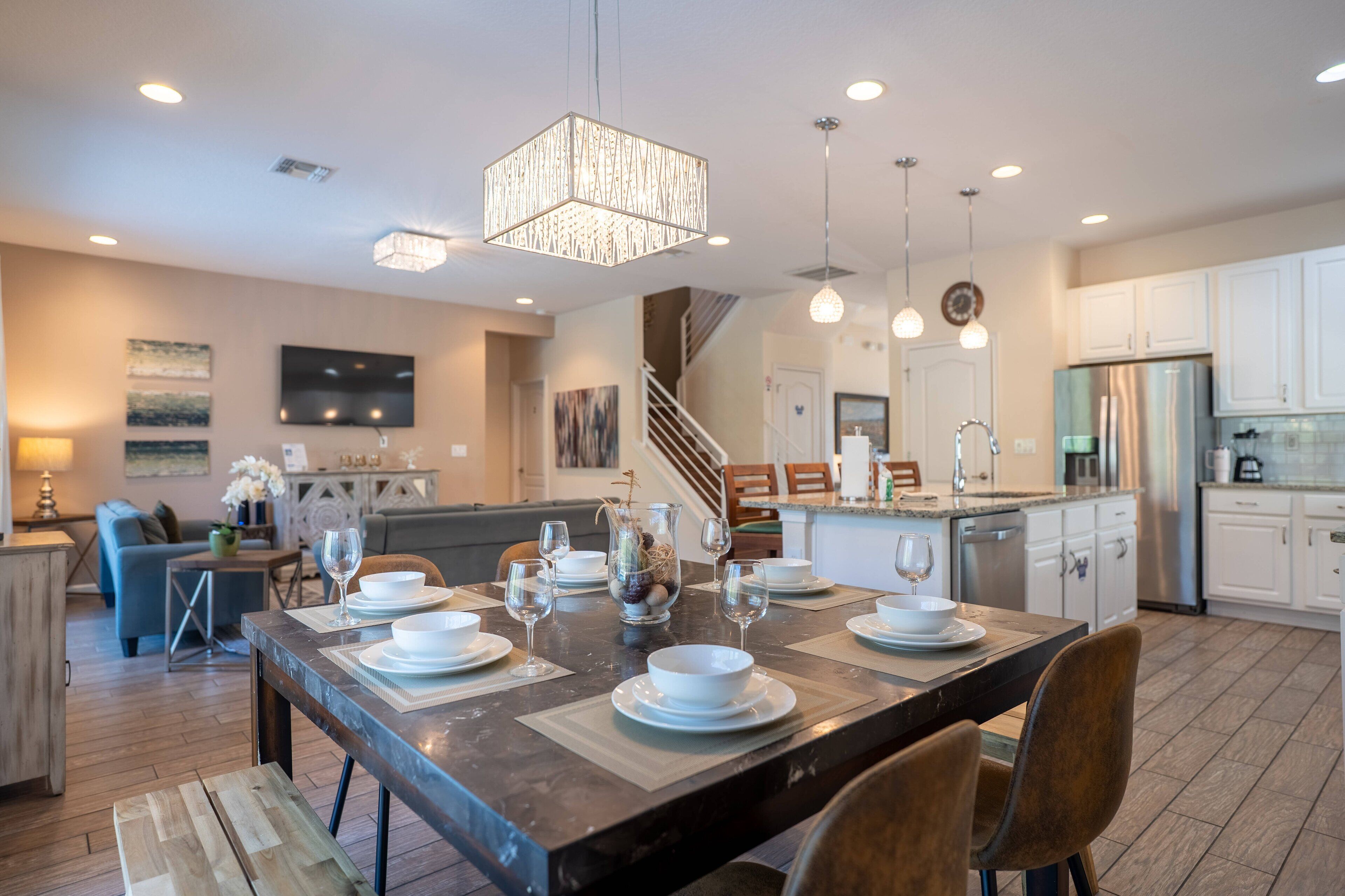 A modern kitchen with white cabinets, a stainless steel refrigerator, and a dining area with a wooden table set for four.
