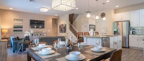 A modern kitchen with white cabinets, a stainless steel refrigerator, and a dining area with a wooden table set for four.