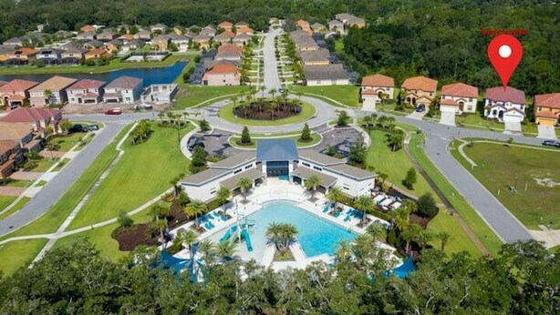 Vue aérienne d’un quartier résidentiel avec une piscine centrale, entourée de maisons et de verdure.