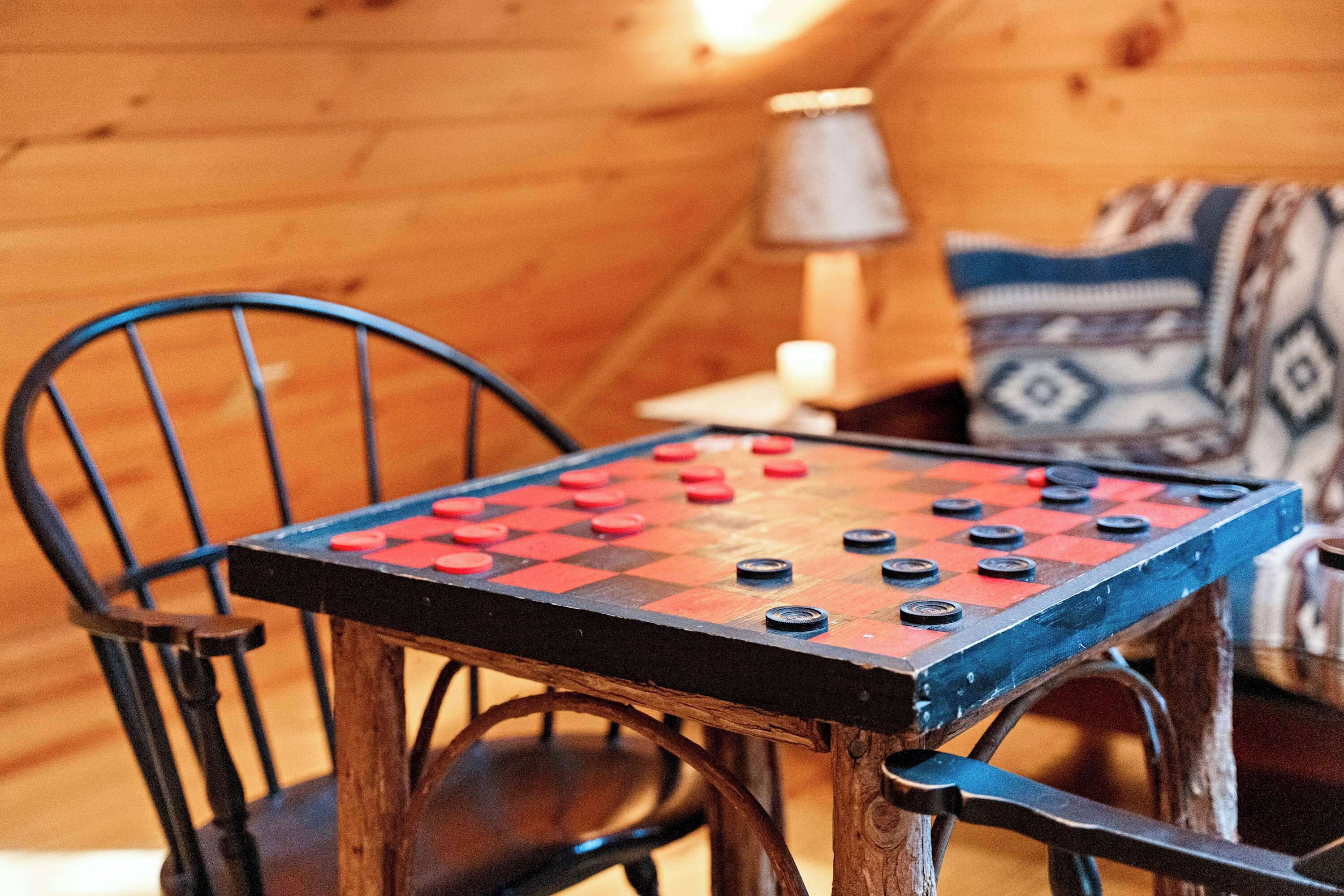 Ein Tisch für Brettspiele mit Schachbrettmuster, Stühle, eine Lampe und ein Kissen mit Muster in einem Holzraum.