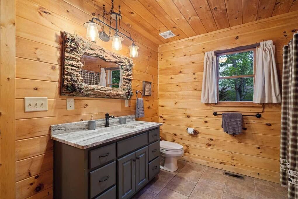A wooden cabin bathroom with a stone-framed mirror, a sink with a marble countertop, and a toilet.