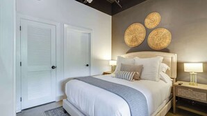 A bedroom with a large bed, two bedside tables, a door, and three wall-mounted decorative items.