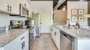 A modern kitchen with white cabinets, granite countertops, stainless steel appliances, and a central island.
