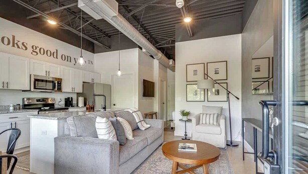 A modern kitchen with stainless steel appliances, a grey sofa, and a round coffee table.