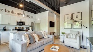 A modern kitchen with white cabinets, stainless steel appliances, and a grey sofa in the living area.