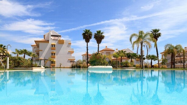 Piscina con el reflejo de un edificio y palmeras.