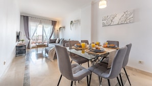 Un comedor moderno con una mesa de vidrio, sillas tapizadas de gris y una mesa para el desayuno con jugo de naranja y pasteles.