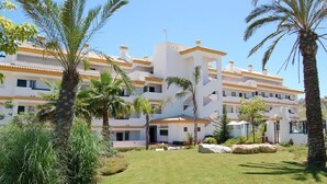 Un hotel de varios pisos con fachada blanca y detalles amarillos, rodeado de palmeras y jardines cuidados.