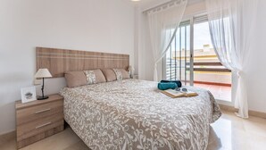 Un dormitorio con una cama grande, una mesita de noche con lámpara y vistas a un balcón.