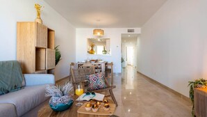 A modern living room with a sofa, a coffee table with snacks, a dining area with a table and chairs, and a kitchen in the background. - Cosy apartment in Manilva with shared pool (Manilva)