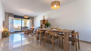 A modern dining area with a wooden table and chairs, a hanging light fixture, and a view through large windows. - Cosy apartment in Manilva with shared pool (Manilva)
