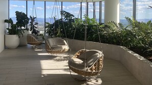 A spacious indoor area with large windows, wicker chairs, and potted plants.
