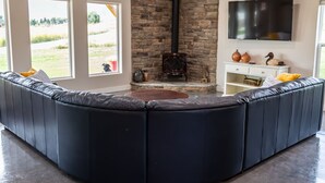 A modern living room with a stone fireplace, a large TV, and a curved black leather sofa. - 3 bedroom guest house with mountain views in Big Horn, Wyoming (Sheridan)