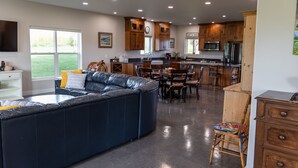 A spacious living area with a large dark-colored sectional sofa, wooden dining table, and chairs. The kitchen features wooden cabinets, a microwave, and a refrigerator. - 3 bedroom guest house with mountain views in Big Horn, Wyoming (Sheridan)