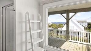 Ein Zimmer mit einer Holterrasse und einer weißen Geländer, einer weißen Leiter sowie Blick auf Häuser und Bäume.