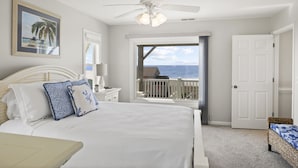 Ein Schlafzimmer mit einem großen Bett, einem Deckenventilator und Blick auf den Ozean durch eine Balkontür.