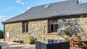 Una casa de pedra amb un espai de pati tancat amb vidre, parets de pedra i una banca de fusta.