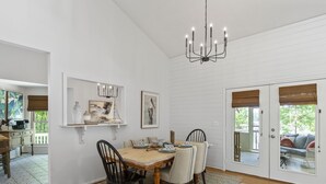 A dining area with a wooden table, chairs, and a chandelier. There are framed artworks on the walls, a window with blinds, and a door leading outside. - Kid Friendly! Upgraded Lake Front Cottage at Lake Martin! 35 Minutes to Auburn!  (Dadeville)