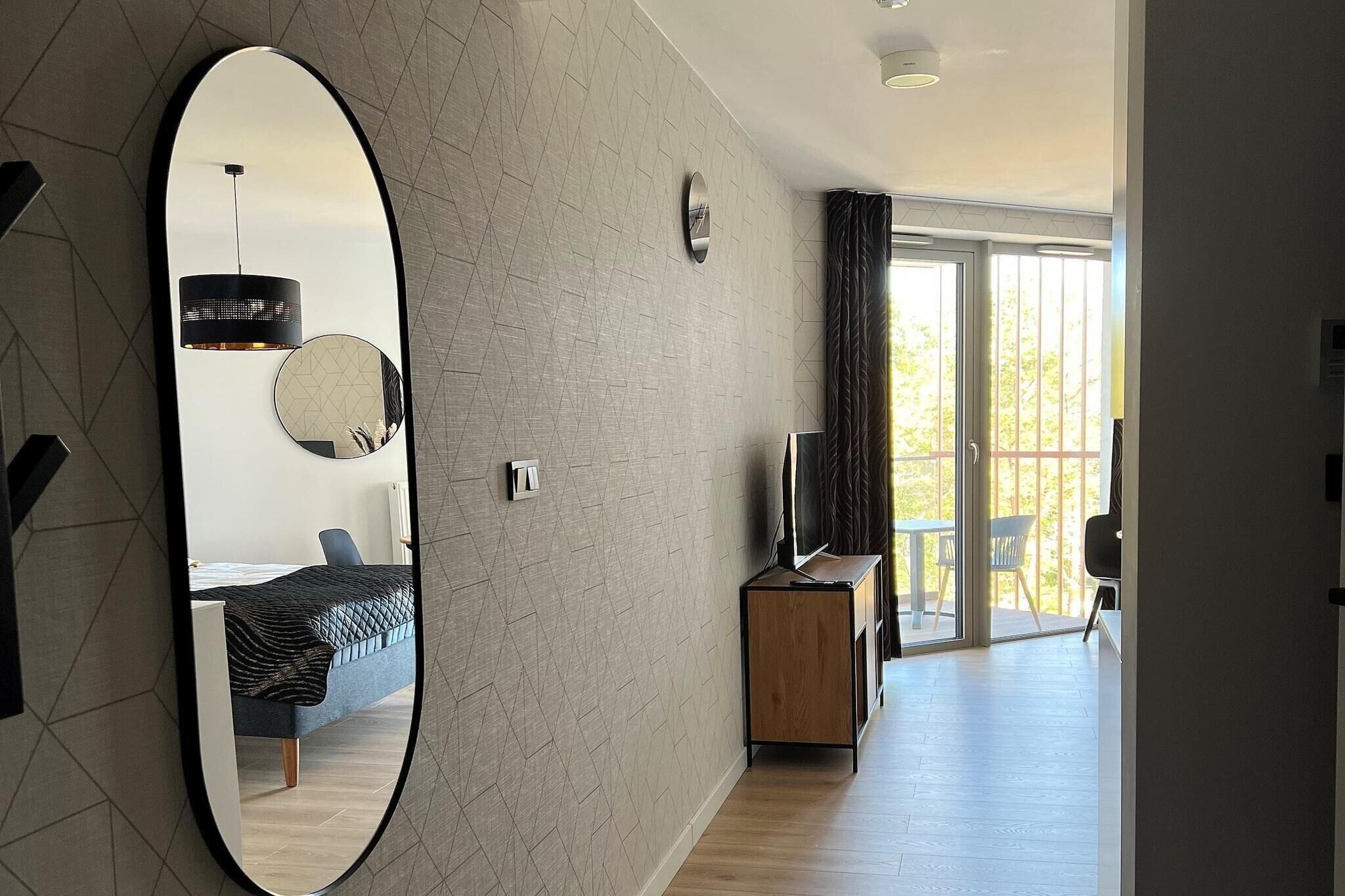 Une chambre d’hôtel moderne dotée d’un grand miroir, d’un lit, d’une télévision et d’un balcon avec vue.