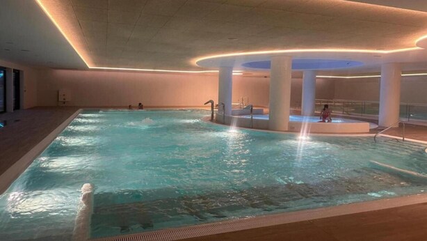 An indoor swimming pool with a central water feature, surrounded by white pillars and a curved ceiling with integrated lighting. - Apartment in Pobierowo near Beach and SPA (Pobierowo)