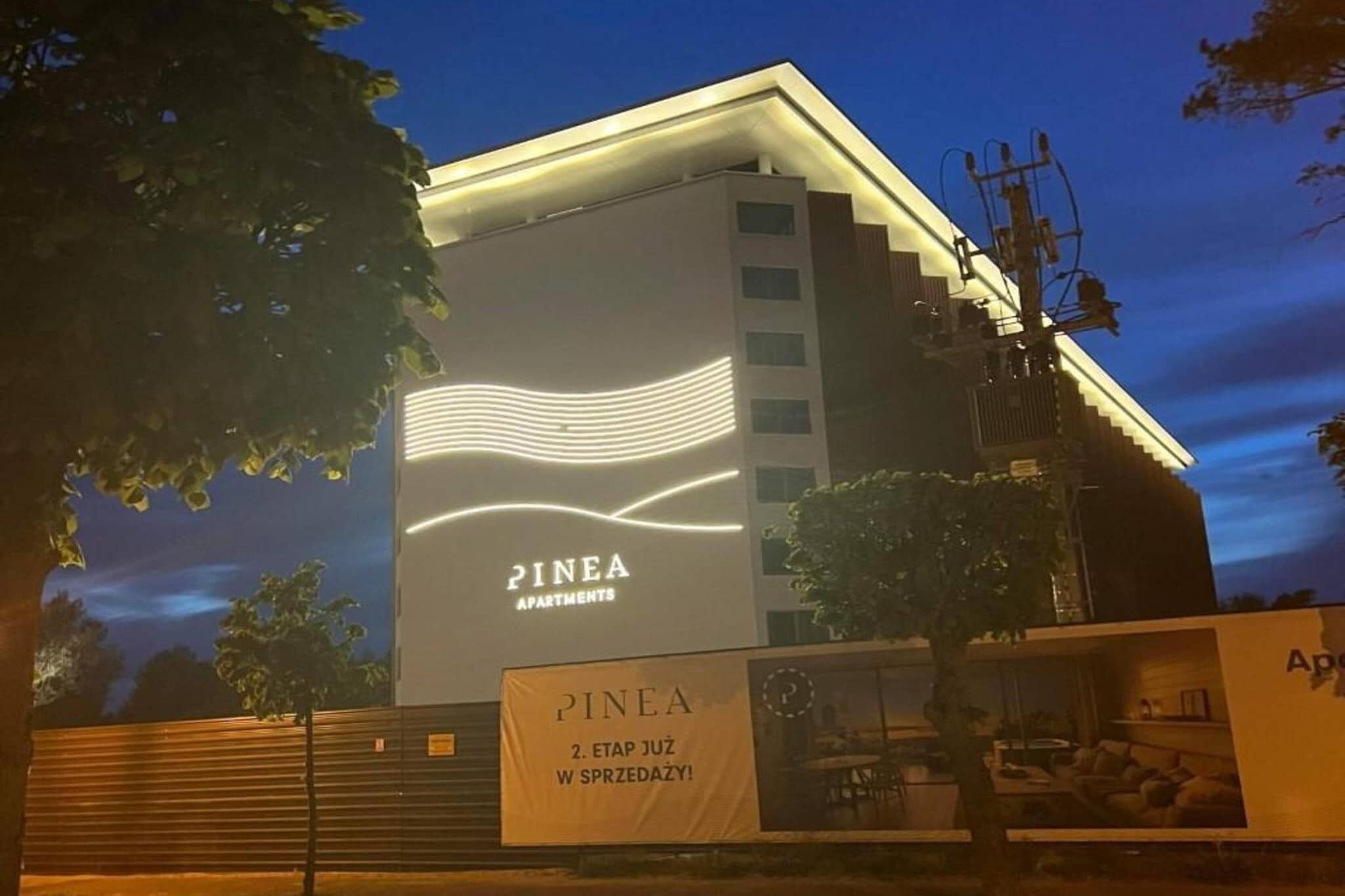 Ein Gebäude mit dem Schild "PINEA APARTMENTS" und einem Banner mit der Aufschrift "PINEA 2. ETAP JUŻ W SPRZEDZĄCY!".