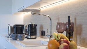 A modern kitchen with a white countertop, a stainless steel kettle, two mugs, a plate of fruit, and two wine glasses. - Apartment in Pobierowo near Beach and SPA (Pobierowo)