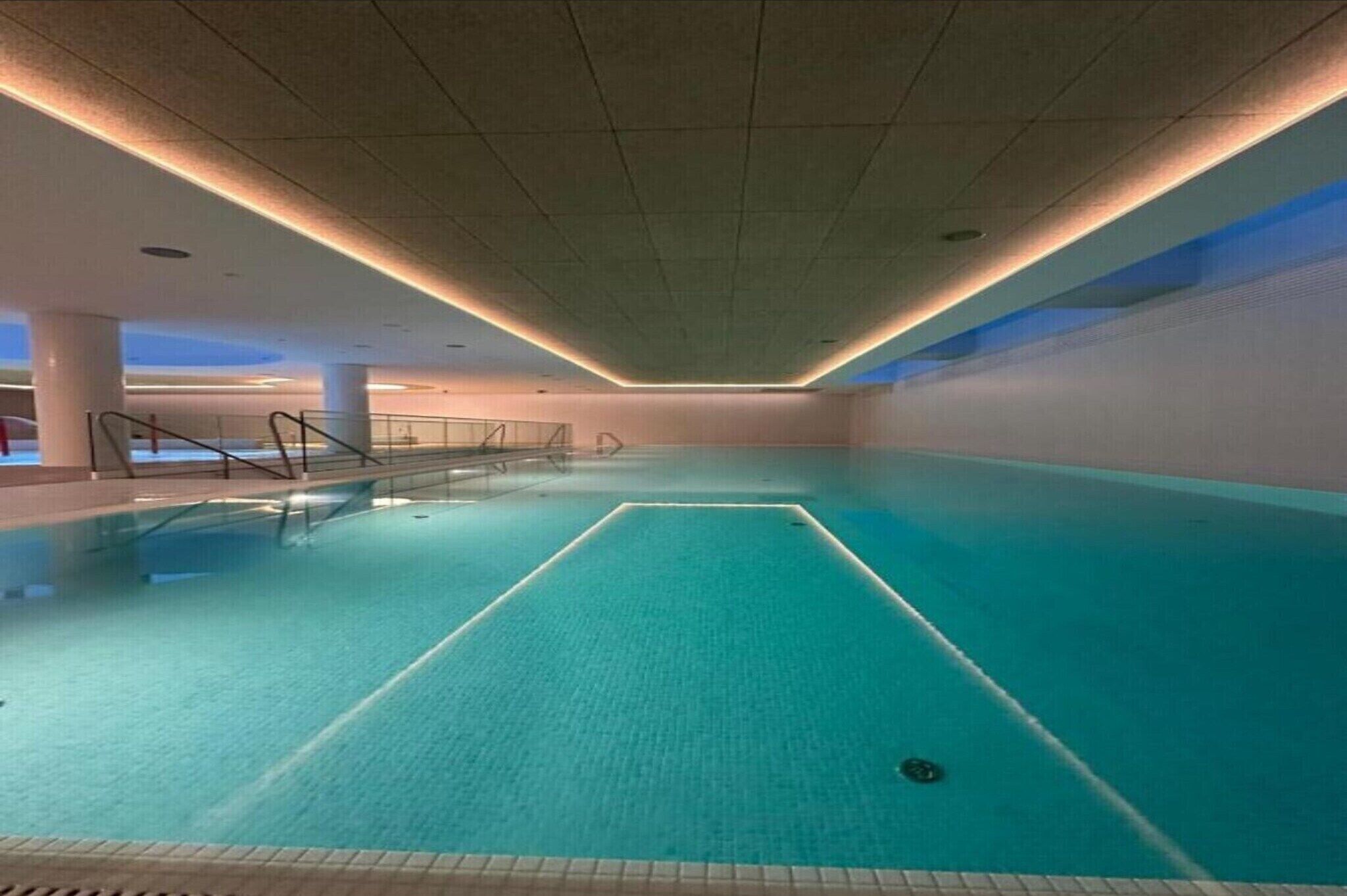 Une piscine intérieure dotée d’un sol carrelé et d’une voie centrale, entourée de murs et d’un plafond équipé d’un éclairage encastré.
